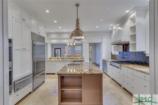 kitchen with hanging light fixtures, light stone countertops, stainless steel appliances, white cabinetry, and a center island with sink