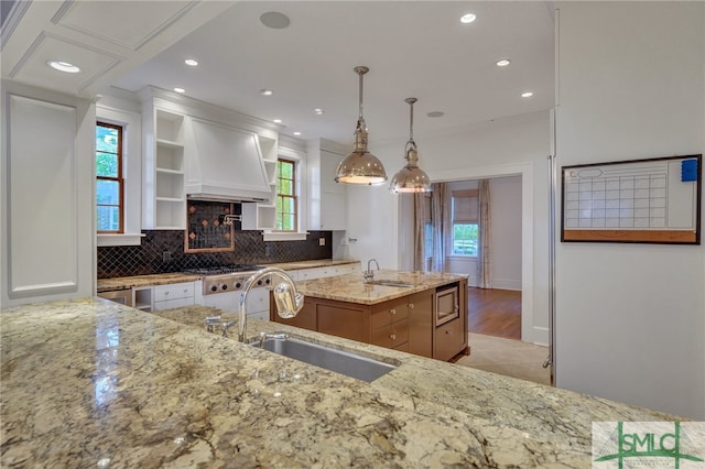 kitchen with hanging light fixtures, light stone countertops, custom exhaust hood, sink, and a multi sided fireplace