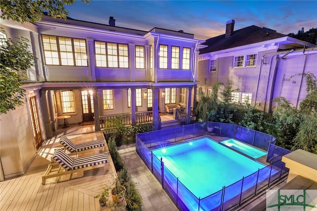 back house at dusk with an in ground hot tub and a wooden deck