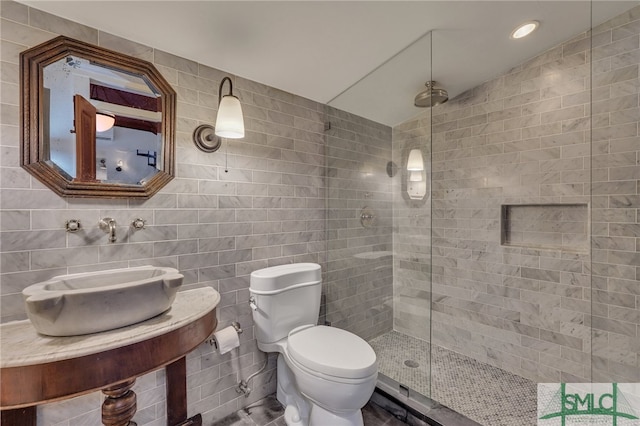 bathroom with tile walls, toilet, tiled shower, and sink