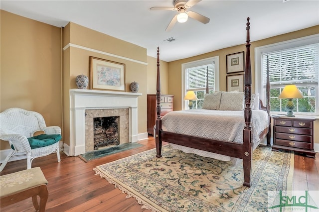 bedroom featuring hardwood / wood-style floors, ceiling fan, and a tile fireplace