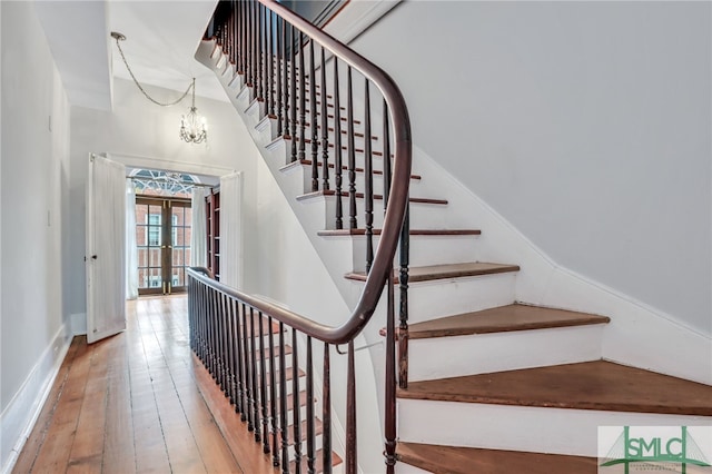 stairs featuring french doors, an inviting chandelier, and hardwood / wood-style floors