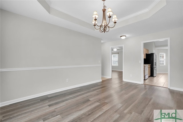 unfurnished dining area with plenty of natural light, a tray ceiling, a chandelier, and wood-type flooring