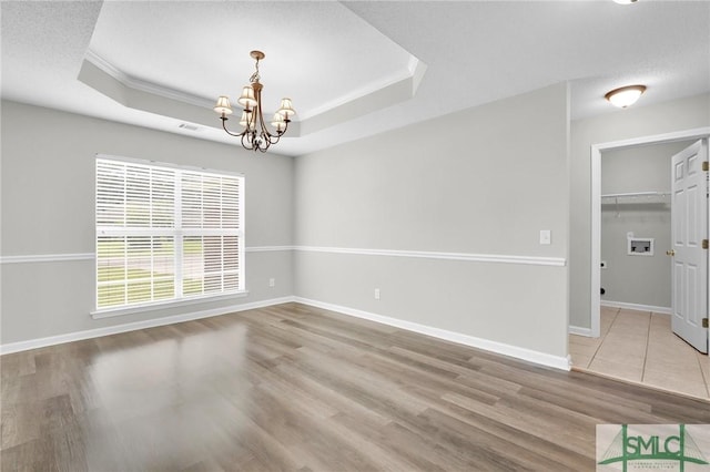 empty room featuring baseboards, a chandelier, ornamental molding, wood finished floors, and a raised ceiling