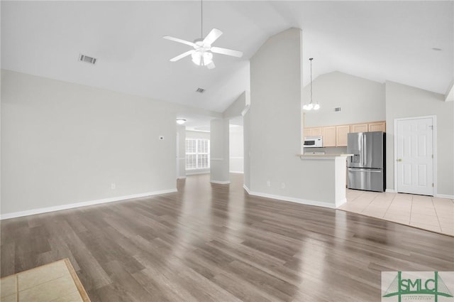 unfurnished living room with light wood-style flooring, ceiling fan with notable chandelier, visible vents, and high vaulted ceiling