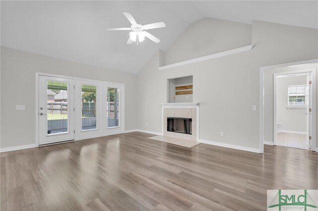 unfurnished living room with plenty of natural light, high vaulted ceiling, wood-type flooring, a tile fireplace, and ceiling fan