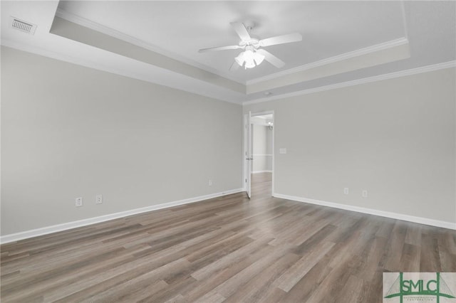 empty room with a tray ceiling, visible vents, and wood finished floors