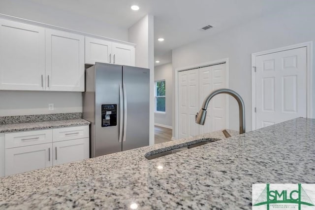 kitchen with stainless steel fridge, white cabinetry, light stone counters, hardwood / wood-style floors, and sink