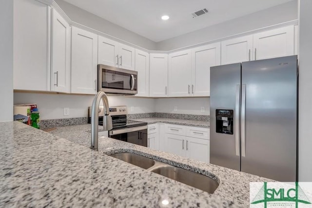 kitchen with white cabinetry, appliances with stainless steel finishes, light stone counters, and sink