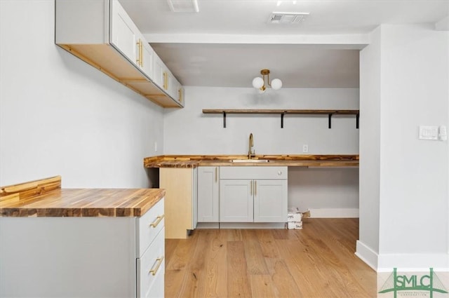 kitchen with butcher block countertops, light wood-type flooring, white cabinetry, and sink