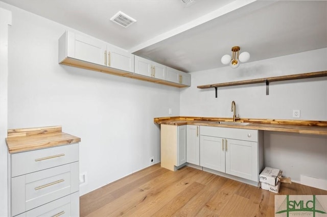 kitchen featuring white cabinets, butcher block counters, sink, and light hardwood / wood-style flooring