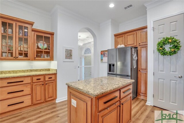 kitchen featuring light stone countertops, stainless steel fridge, light wood-type flooring, and crown molding