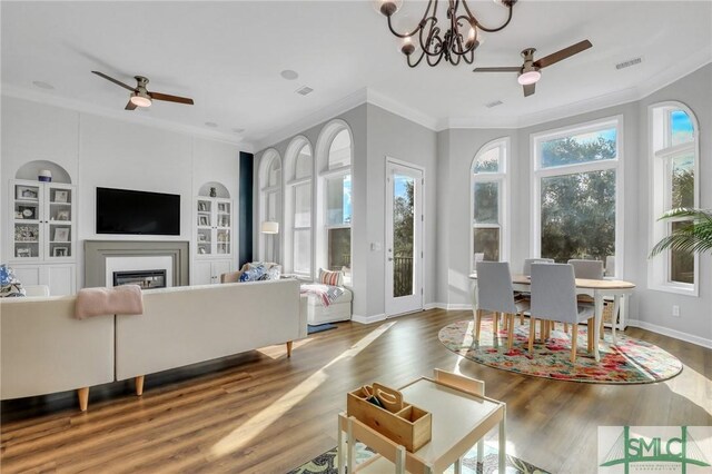 living room featuring hardwood / wood-style flooring, built in shelves, ornamental molding, and ceiling fan with notable chandelier