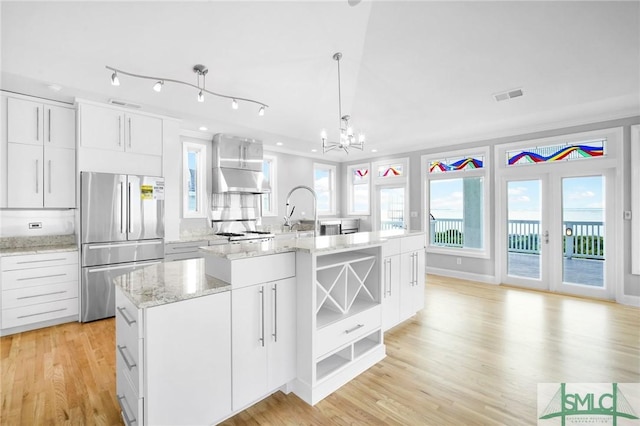 kitchen with an inviting chandelier, stainless steel built in refrigerator, pendant lighting, a center island with sink, and white cabinets