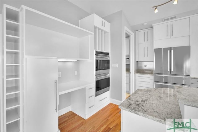 kitchen featuring white cabinets, light hardwood / wood-style floors, light stone countertops, and stainless steel appliances