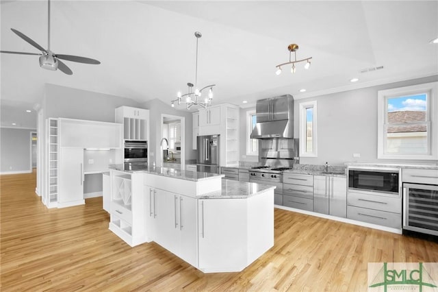 kitchen featuring stainless steel appliances, wall chimney range hood, a spacious island, decorative light fixtures, and white cabinets