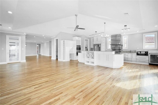 unfurnished living room with ceiling fan with notable chandelier, vaulted ceiling, light hardwood / wood-style floors, and wine cooler