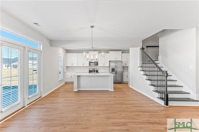 kitchen featuring white cabinetry, pendant lighting, a center island with sink, appliances with stainless steel finishes, and light wood-type flooring