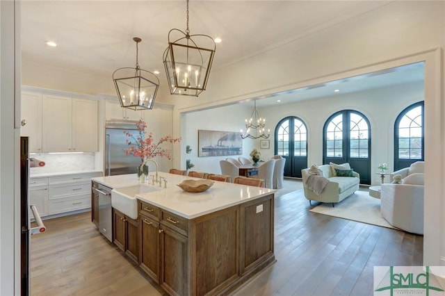 kitchen featuring pendant lighting, backsplash, an island with sink, appliances with stainless steel finishes, and white cabinetry