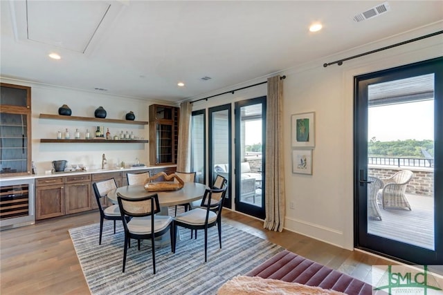 dining space with bar area, light hardwood / wood-style floors, wine cooler, and crown molding