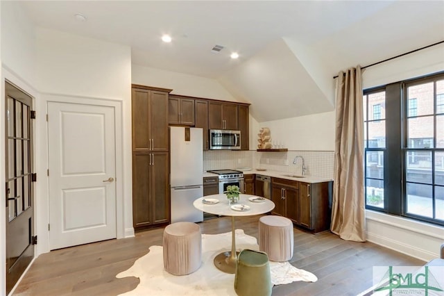 kitchen featuring decorative backsplash, a wealth of natural light, stainless steel appliances, vaulted ceiling, and sink