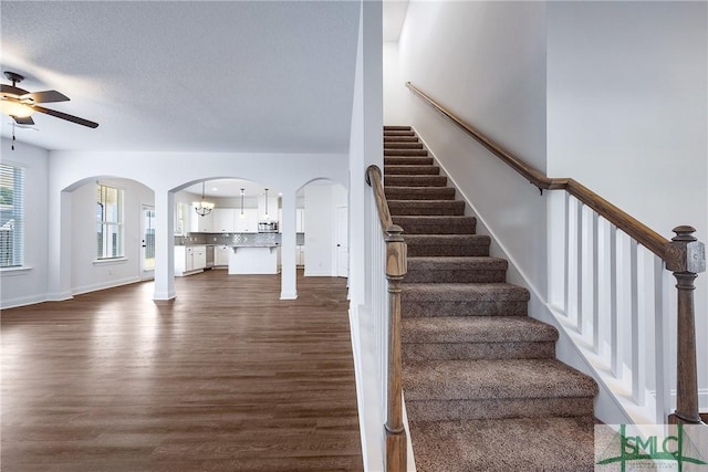 stairs featuring hardwood / wood-style flooring, ceiling fan with notable chandelier, and a textured ceiling