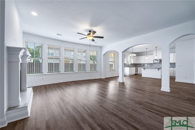 unfurnished living room featuring a textured ceiling, plenty of natural light, dark hardwood / wood-style flooring, and ceiling fan with notable chandelier