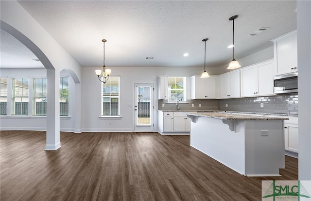 kitchen with white cabinetry, light stone countertops, dark hardwood / wood-style floors, pendant lighting, and a kitchen island