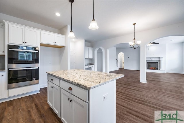 kitchen featuring dark hardwood / wood-style floors, double oven, decorative light fixtures, white cabinets, and ceiling fan with notable chandelier