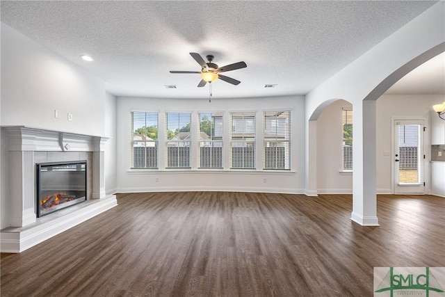 12 Cottonfield Dr, Guyton, GA 31312 - unfurnished living room with a ceiling fan, dark wood-type flooring, a textured ceiling, arched walkways, and a glass covered fireplace
