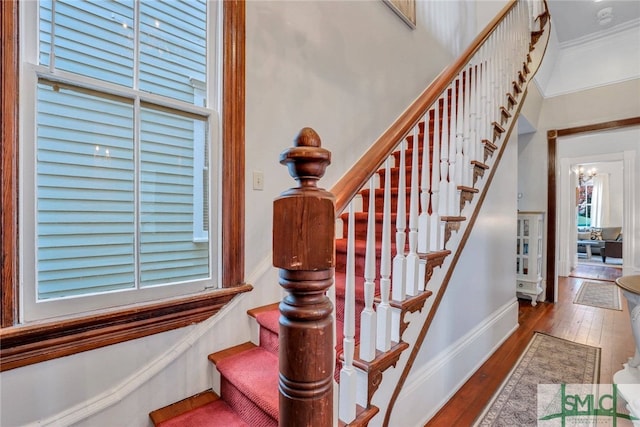 stairs featuring hardwood / wood-style floors, ornamental molding, and an inviting chandelier