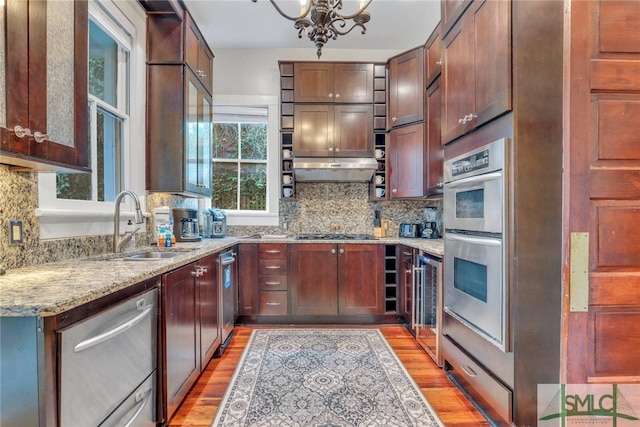 kitchen featuring light stone countertops, stainless steel appliances, sink, light hardwood / wood-style flooring, and a chandelier