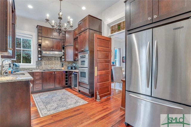 kitchen featuring light stone countertops, sink, an inviting chandelier, pendant lighting, and appliances with stainless steel finishes