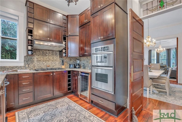 kitchen featuring hardwood / wood-style floors, light stone countertops, appliances with stainless steel finishes, beverage cooler, and a chandelier