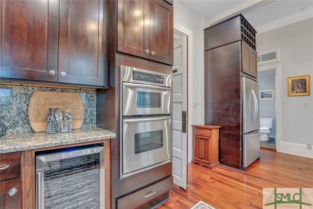 kitchen featuring light stone countertops, appliances with stainless steel finishes, tasteful backsplash, light hardwood / wood-style floors, and beverage cooler