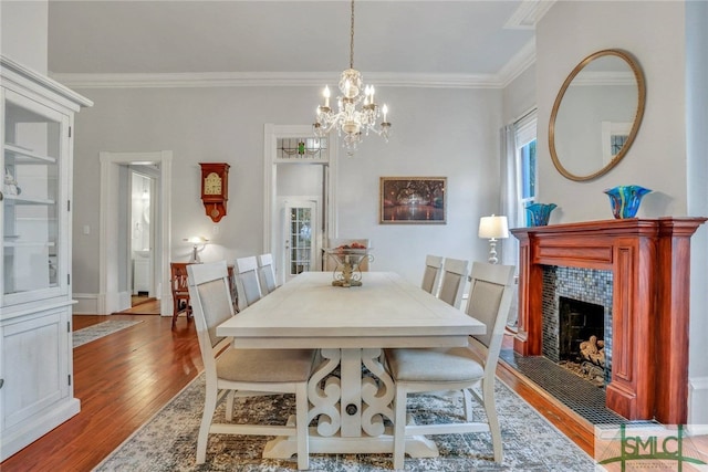 dining area with a tile fireplace, crown molding, an inviting chandelier, and light wood-type flooring