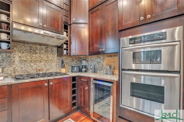 kitchen featuring backsplash, light stone countertops, appliances with stainless steel finishes, light hardwood / wood-style floors, and beverage cooler