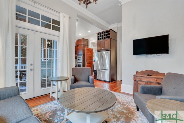 living room featuring a chandelier, french doors, light wood-type flooring, and ornamental molding