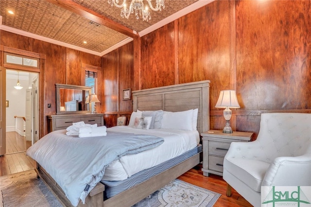 bedroom featuring wood walls, wood-type flooring, a notable chandelier, and ornamental molding