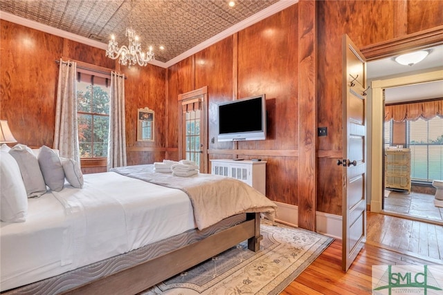 bedroom with light hardwood / wood-style floors, an inviting chandelier, multiple windows, and crown molding