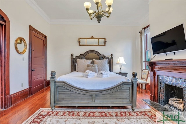 bedroom featuring a tiled fireplace, crown molding, a notable chandelier, and light wood-type flooring