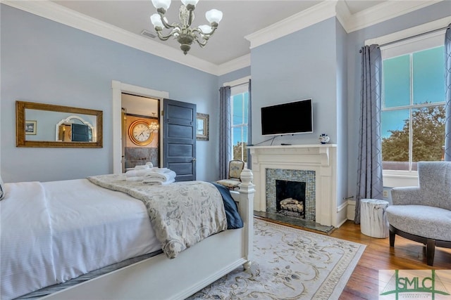 bedroom with hardwood / wood-style floors, crown molding, a fireplace, and an inviting chandelier