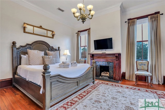 bedroom featuring a tile fireplace, wood-type flooring, ornamental molding, and a notable chandelier