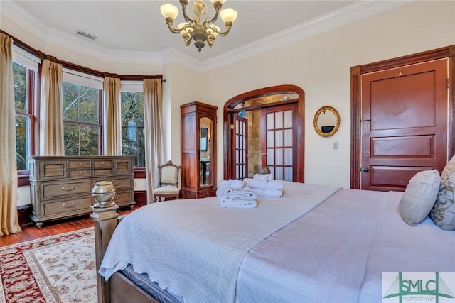 bedroom featuring hardwood / wood-style flooring, french doors, ornamental molding, and an inviting chandelier