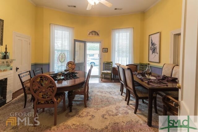 dining area with wood-type flooring, ornamental molding, ceiling fan, and a fireplace