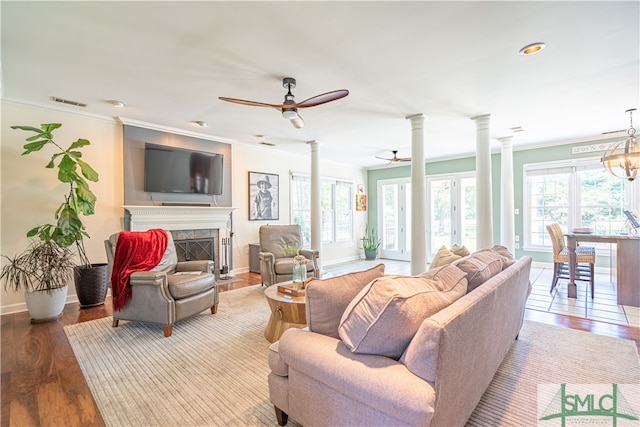 living room featuring ceiling fan with notable chandelier, light hardwood / wood-style flooring, crown molding, and a tiled fireplace