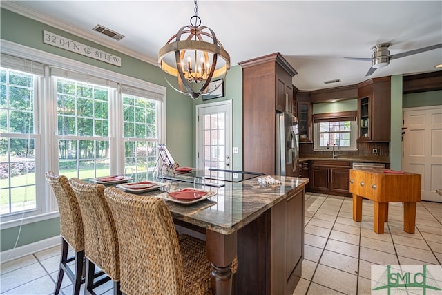 kitchen with ceiling fan with notable chandelier, crown molding, dark stone countertops, tasteful backsplash, and stainless steel appliances