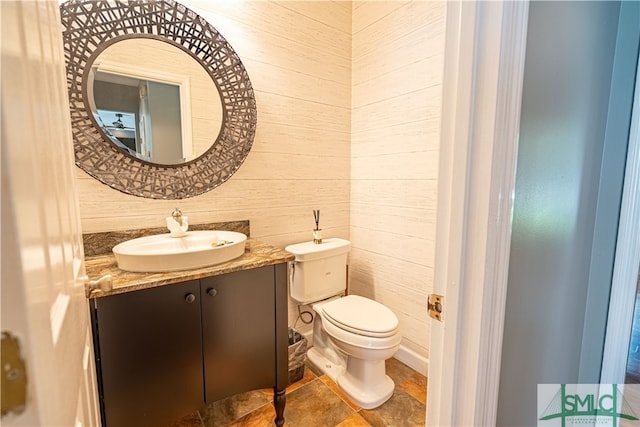 bathroom featuring vanity, wood walls, and toilet