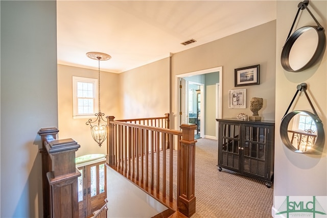 hall featuring carpet, ornamental molding, and an inviting chandelier