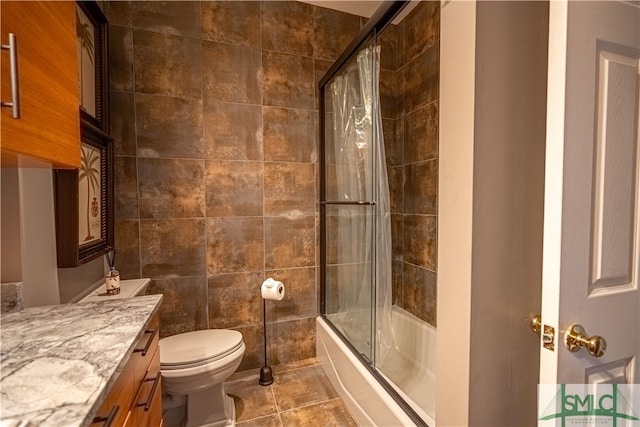 full bathroom featuring tile patterned floors, toilet, shower / bath combination with glass door, vanity, and tile walls